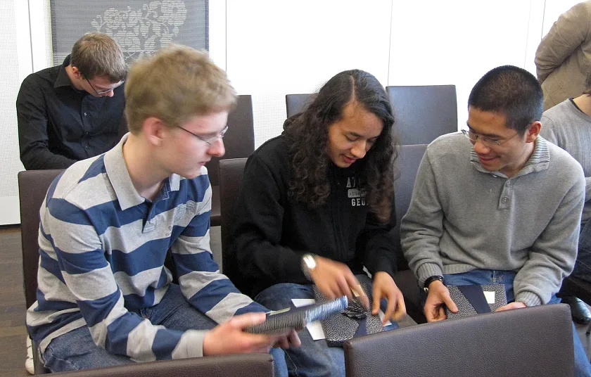 Die drei Preisträger (von links) Fabian Henneke, Danial Sanusi und Xianghui Zhong beim Auswickeln der Bücher, die ihnen die Senatorin geschenkt hat