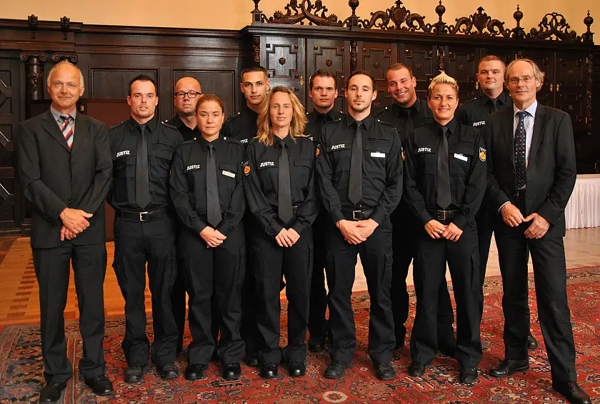 Justizstaatsrat Matthias Stauch (r.) und JVA-Leiter Dr. Carsten Bauer mit den neuen Justizvollzugsbediensteten im Festsaal des Bremer Rathauses