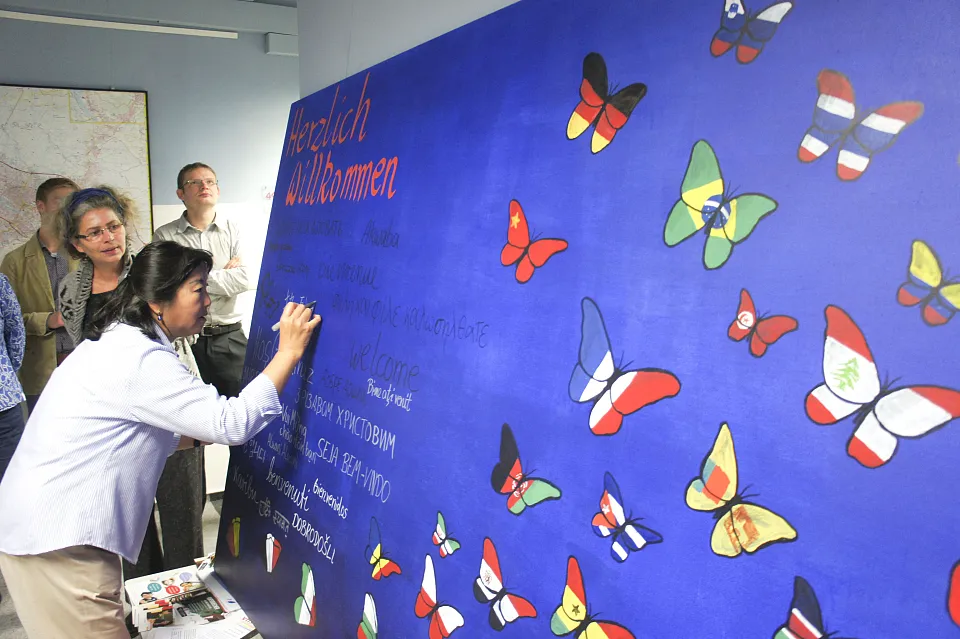 VHS-Dozentin  Rong Fang Cao bringt chinesische Schriftzeichen auf dem Bild von Sonja Schadwinkel (dahinter stehend) an. 