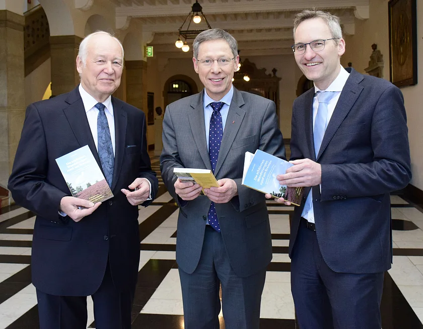 Autor Harald Witt (li.) und Verleger Florian Isensee (re.) überreichen Bürgermeister Carsten Sieling das neue Wanderbuch