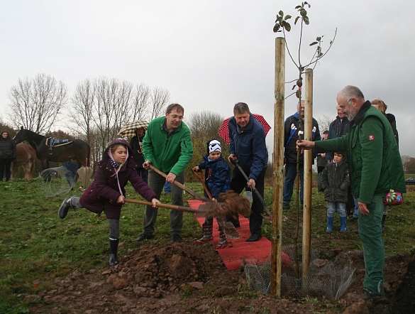 Senator Joachim Lohse (mi.) mit den Kindern Justus und Pia Anders und weitere Helfer pflanzen den ersten Obstbaum der Streuobstwiese
