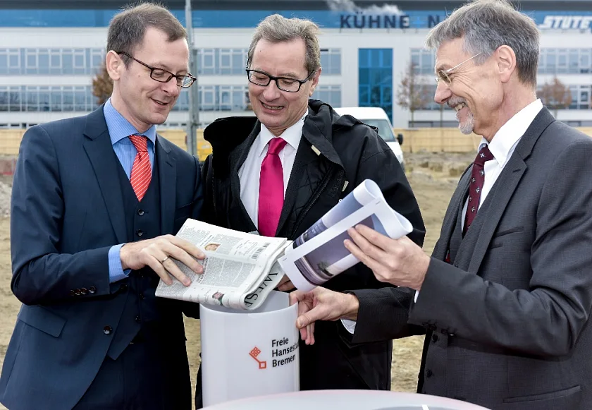 Baupläne, eine Zeitung, Fotos und ein 3D-Modell: (v.l.n.r.) Martin Günthner, Senator für Wirtschaft, Arbeit und Häfen, Charles Champion, Executive Vice President Engineering bei Airbus, und Michael Göbel, Geschäftsführer Kaufmännische Dienste bei der WFB Wirtschaftsförderung Bremen GmbH, befüllen gemeinsam die Zeitkapsel, die in den Baugrund des EcoMaT versenkt wurde.