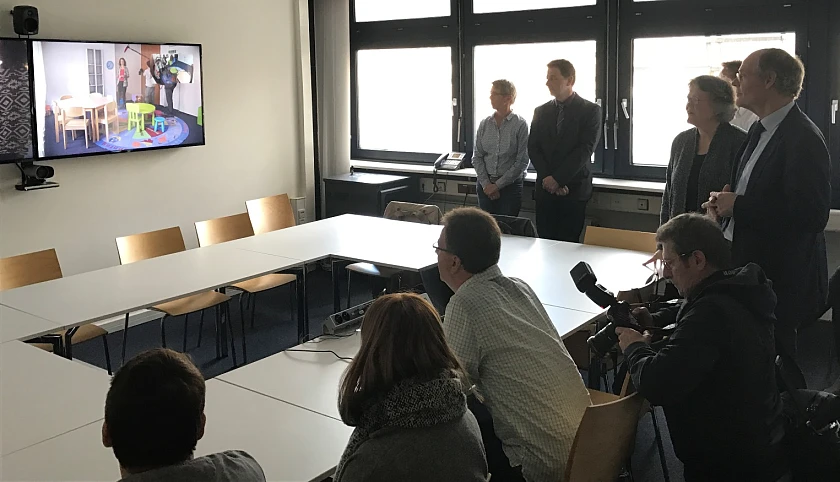 Staatsrat Stauch und Landesfrauenbeauftragte Hauffe (stehend, 1. u. 2. v.r.) stellen zusammen mit Amtsgerichtspräsidentin Wolff (im Monitorbild) die neue Videovernehmungsanlage vor