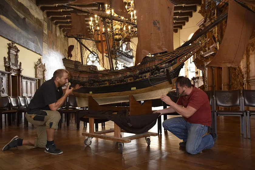 Alexey Hübscher, Hausmeister im Rathaus (re.), und der Holzrestaurator Manfred Hübner aus Bremen, hängten heute in der Oberen Rathaushalle das rund 250 kg schwere historische Modellschiff einer Fregatte aus dem 17. Jahrhundert ab. Aufgestellt auf einer Stellage kann es hier von den Gästen des Rathauses ab dem 4. August bis zum 19. November aus einer ganz unüblichen Perspektive besichtigt werden. Foto: Senatspressestelle