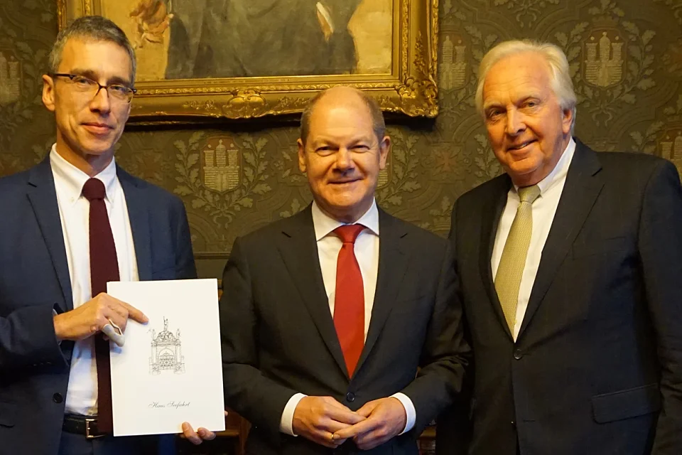 Der Verwaltende Vorsteher von Haus Seefahrt, Heiner Dettmer (rechts), und der 1. Schaffer und SWB-Vorstandsvorsitzende, Dr. Torsten Köhne (links), überreichen Hamburgs Erstem Bürgermeister Olaf Scholz die Einladung zur Schaffermahlzeit. 