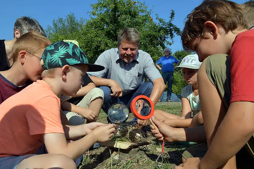 Umweltbildung im Bremer Osten: Senator Lohse besucht das Kinderferienprogram des NABU in der Vahr und zeigt Kindern, wie man mit Lupen Feuer macht und dass es daher gefährlich ist, Glas in der Natur liegen zu lassen
