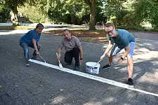 Drei Kollegen, die einen Strich am Boden erneuern: 