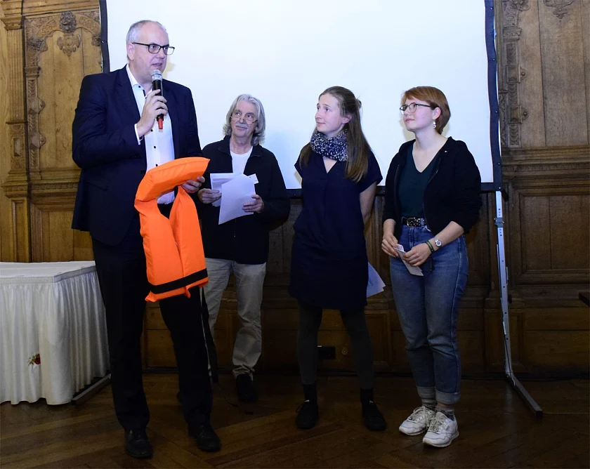 Bürgermeister Bovenschulte nimmt von drei Aktivistinnen der Initiative Seebrücke eine rote Rettungsweste entgegen. Die BEK unterstützt deren Engagement im  Mittelmeer, um Flüchtlinge vor dem Ertrinken zu retten.