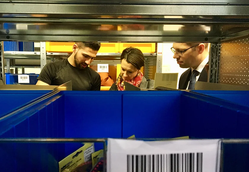 Ein Blick durchs Regal. Ein Auszubildender präsentiert Lagerhaltung mit Listen. 