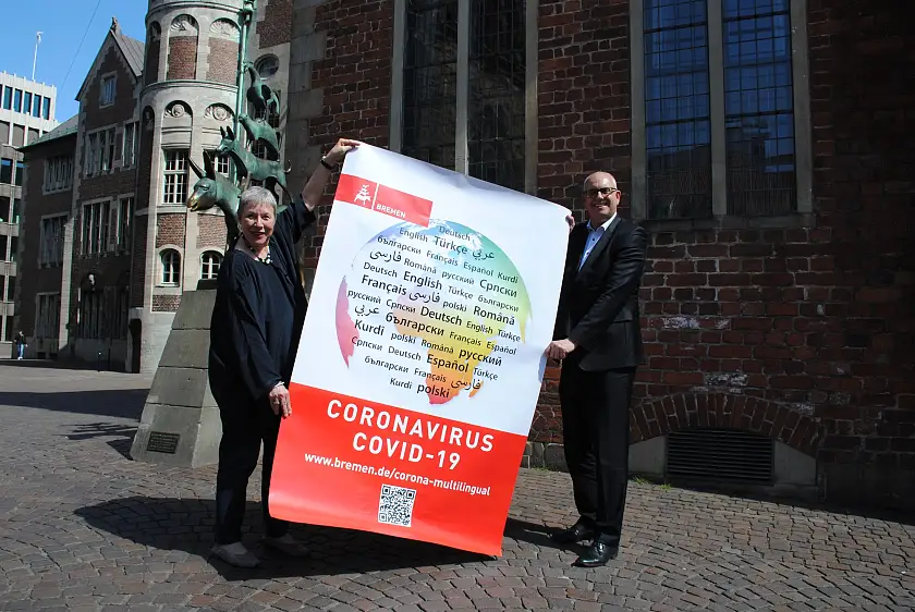 Projektkoordinatorin Birgitt Rambalski, in Nicht-Corona-Zeiten Protokollchefin im Rathaus, und Bürgermeister Andreas Bovenschulte präsentieren vor den Bremer Stadtmusikanten eines der Großplakate, mit denen Bremen ab dem 2. Juni an 300 Stellen in der Stadt mehrsprachig für das Einhalten der Corona-Regeln wirbt
