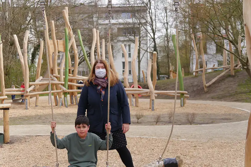 Elias (7) probiert die Schaukel auf dem Spielplatz Tieckstraße aus, assistiert von Senatorin Stahmann
