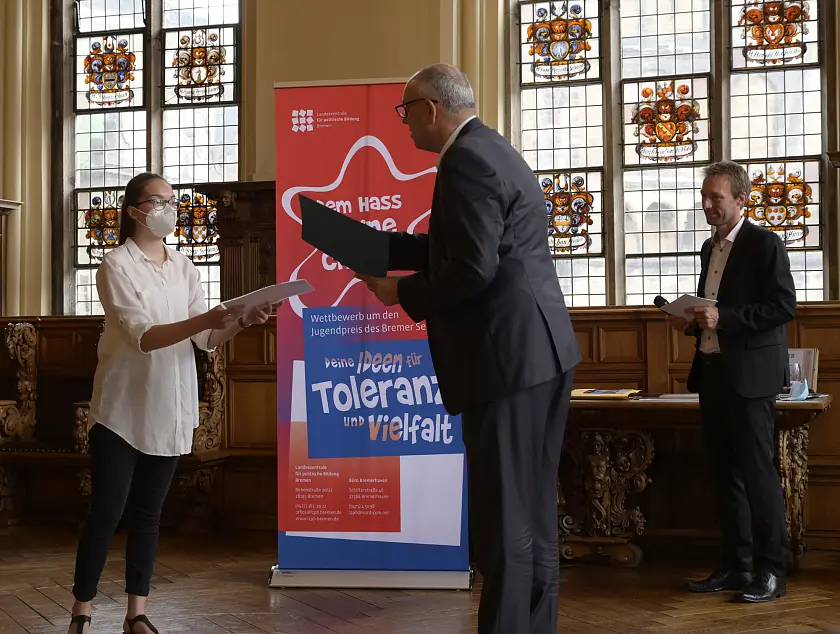 Ausgezeichnet für ihr Video „This Society’“ wurden Emma Sieling  und Laura Zeppenfeld (nicht im Bild) von Bürgermeister Andreas Bovenschulte (Mitte) mit dem Senatspreis. Mit im Bild: Dr. Thomas Köcher, Leiter der Landeszentrale für politische Bildung Bremen. Foto: Senatspressestelle