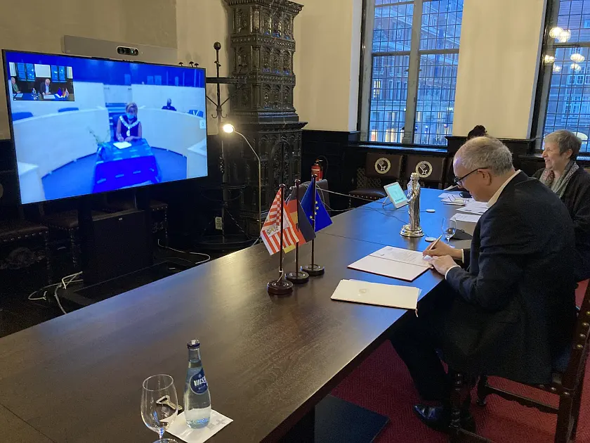 Der Moment der Unterzeichnung: Windhoeks Bürgermeisterin Sade Gawanas auf dem Bildschirm und Bürgermeister Dr. Andreas Bovenschulte in der Wittheitsstube des Bremer Rathauses. Mit dabei die Protokollchefin des Rathauses, Birgitt Rambalski (rechts). Foto: Senatspressestelle