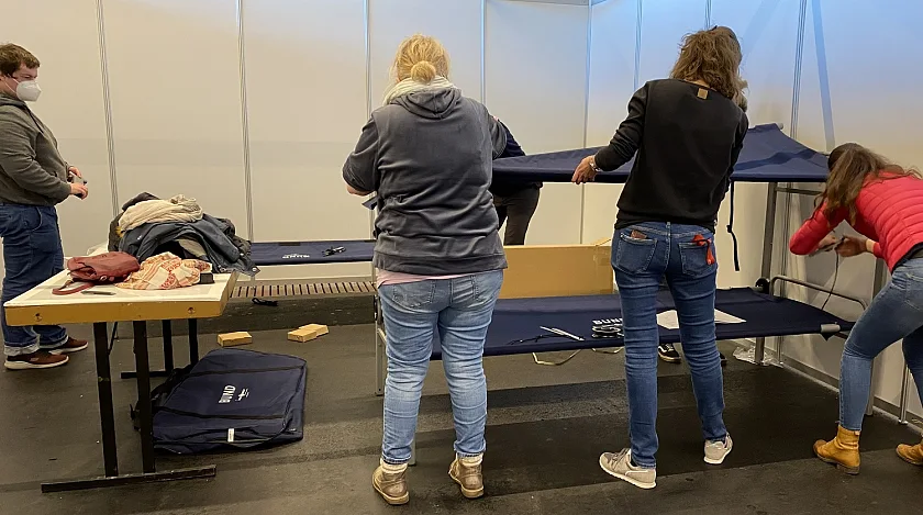Ehrenamtliche unterstützen die DRK-Kräfte beim Aufbau der Betten in der Messehalle 7. Foto: Sozialressort