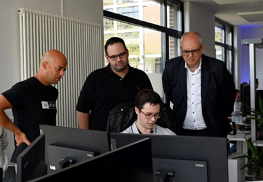 Die Geschäftsführer von JUSTADD AI, Roland Becker (links) und Julian Moeser (Mitte) sowie ihr Mitarbeiter Aljoscha Niazi-Shahabi (sitzend) erläutern Bürgermeister Andreas Bovenschulte die Entwicklung von KI-basierten Programmen. Foto: Senatspressestelle