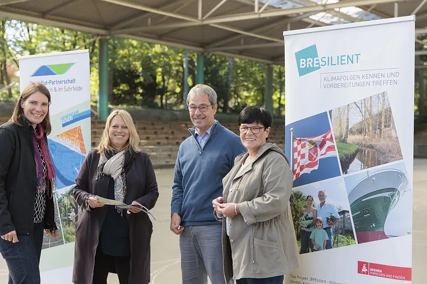 Mitglieder der neuen Sturmflutpartnerschaft in Bremen (v. l.): Dr. Lucia Herbeck und Dr. Maike Schaefer, Senatorin für Klimaschutz, Umwelt, Mobilität, Stadtentwicklung und Wohnungsbau, sowie Elke Müller, Vorsitzende des Kleingartenvereins Gartenfreunde Weserlust, und Axel Viereck, Vorstand des Vereins FC Union60 Bremen. Foto: BREsilient, Fotograph: Jörg Sarbach