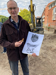 Dr. Dieter Bischop zeigt vor der Rekonstruktionszeichnung der Bremer Kogge eine der gefundenen Kalfaterklammern. Foto: Kulturressort