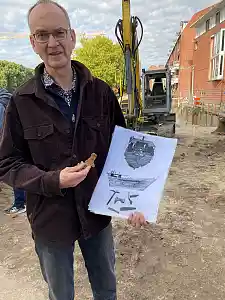 Dr. Dieter Bischop zeigt vor der Rekonstruktionszeichnung der Bremer Kogge eine der gefundenen Kalfaterklammern. Foto: Kulturressort