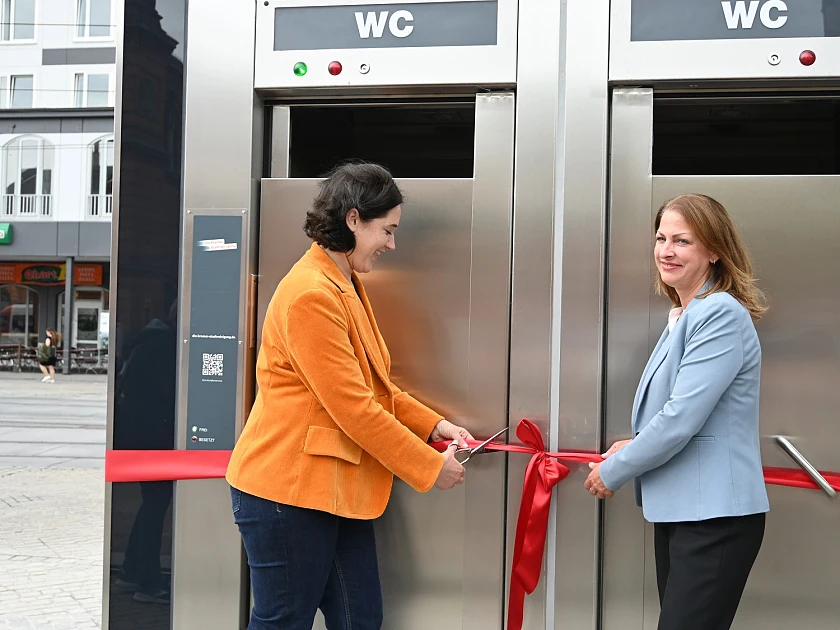 Ab sofort können die vier Toiletten genutzt werden, kostenlos und rund um die Uhr. Senatorin Kathrin Moosdorf durchtrennt gemeinsam mit DBS-Vorständin Daniela Einslein symbolisch ein Band zur Eröffnung. Foto: Umweltressort