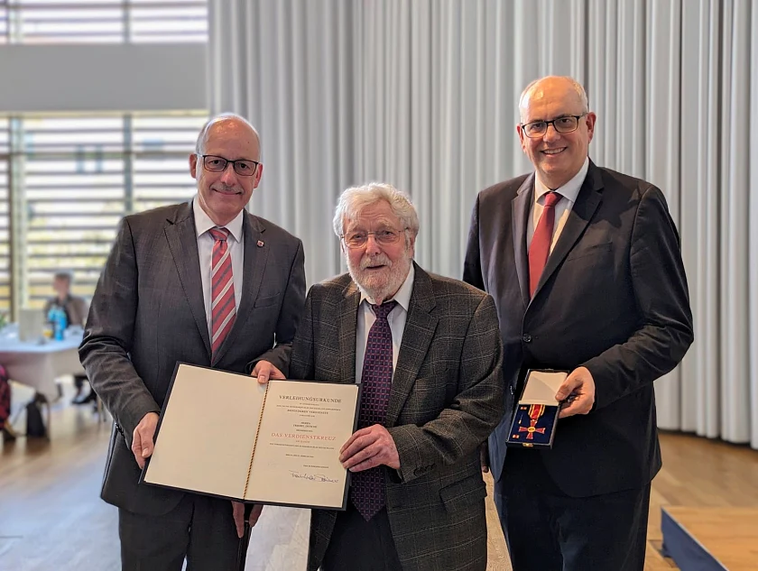 Bremerhavens Stadtverordnetenvorsteher Torsten von Haaren (links) und der Präsident des Bremer Senats, Bürgermeister Andreas Bovenschulte (rechts), überreichten im Deutschen Auswandererhaus das Bundesverdienstkreuz am Bande an Friedel Ditsche. Foto: Magistratspressestelle / Anja Müdeking