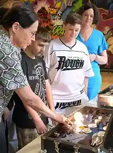 Katja Muchow vom BUND Bremen (links) zeigt Yusuf und Max vom DRK Jugendzentrum Findorff und Umweltsenatorin Kathrin Moosdorf mit einem Lampenkoffer, wie unterschiedlich der Stromverbrauch - je nach Leuchtmittel - ausfallen kann. Foto: ener:freizi / Michael Bahlo