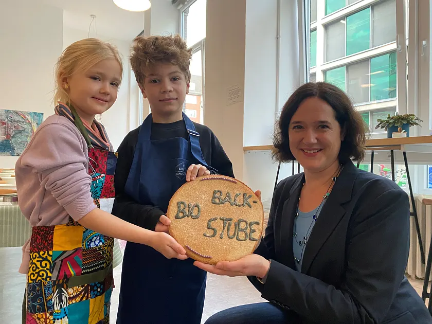 Senatorin Kathrin Moosdorf bricht zusammen mit Lina und Matti den Keks. Damit ist die BioBackstube 2024 eröffnet. 