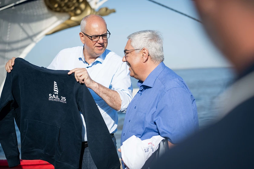 Oberbürgermeister Melf Grantz übergibt Bremens Bürgermeister, Andreas Bovenschulte, vor der Einlaufparade den offiziellen Hoodie der SAiL Bremerhaven 2025. Foto: Magistratspressestelle / Arnd Hartmann