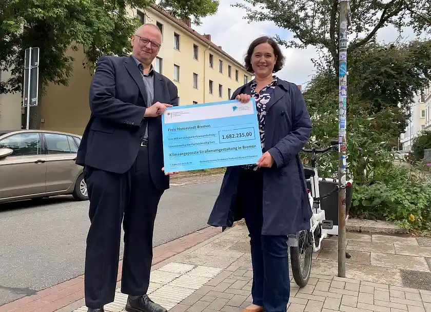 Staatssekretär Dr. Olaf Joachim überreicht einen Check an Senatorin Kathrin Moosdorf. Mit dem Geld sollen Bäume in der Delme- und der Scharnhorststraße zu baumfreundlichen Straßen werden. 