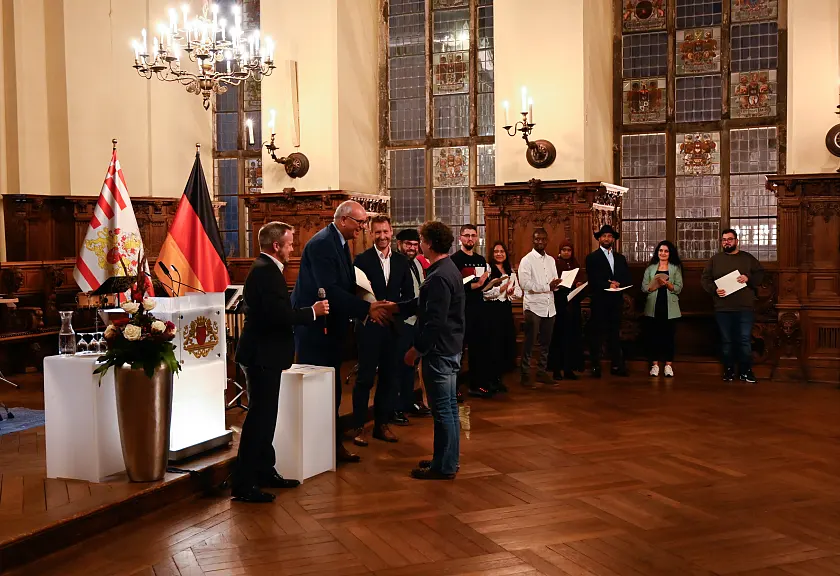 Bürgermeister Andreas Bovenschulte überreicht eine Einbürgerungsurkunde.