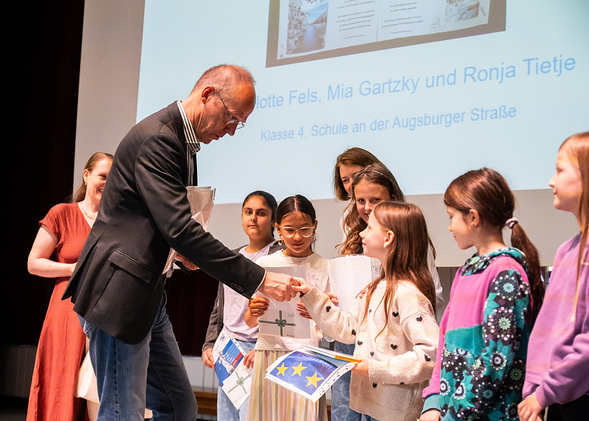 Senator Mark Rackles übergibt den Preis für die beste Bildarbeit zum Thema  Wir machen uns die Welt, wie sie uns gefällt! an die vierte Klasse  der Schule an der Augsburger Straße.